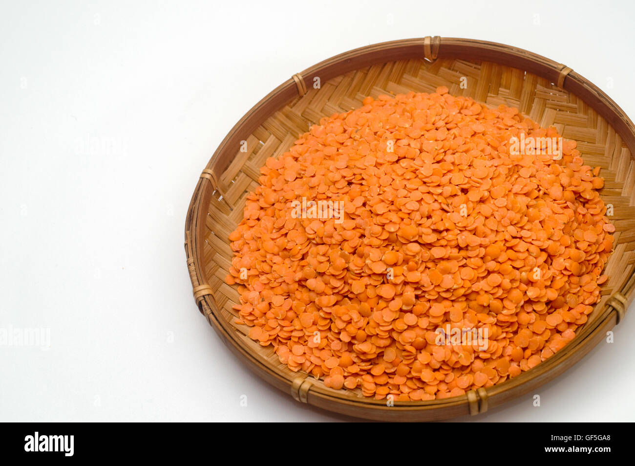 Organici di lenticchie rosse (Lens culinaris) in un piatto di paglia su sfondo bianco Foto Stock