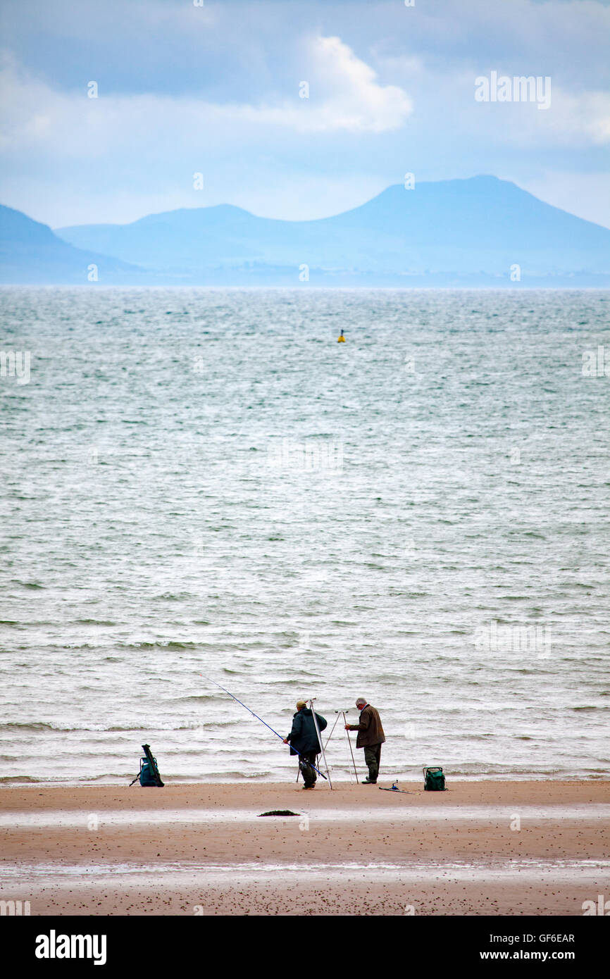 Due pescatori la pesca sulla spiaggia di newborough warren, Anglesey, Galles, nel Regno Unito con la penisola llyn montagne litoranee della distanza Foto Stock