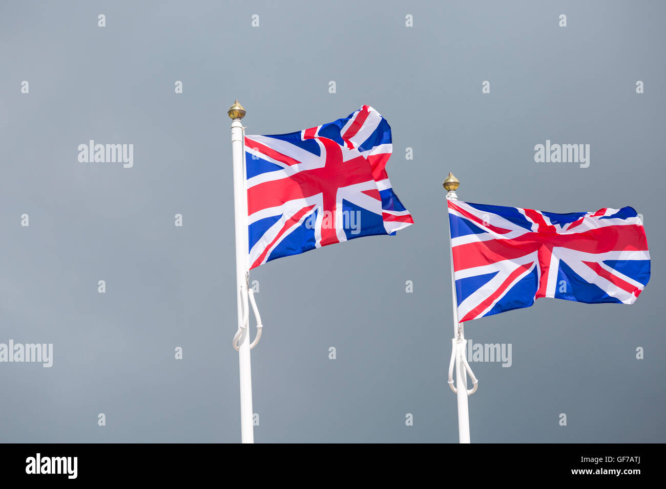 Due Union Jack Flag su pali di bandiera che soffia nella brezza contro tempestoso cieli grigi a Dorset in luglio Foto Stock