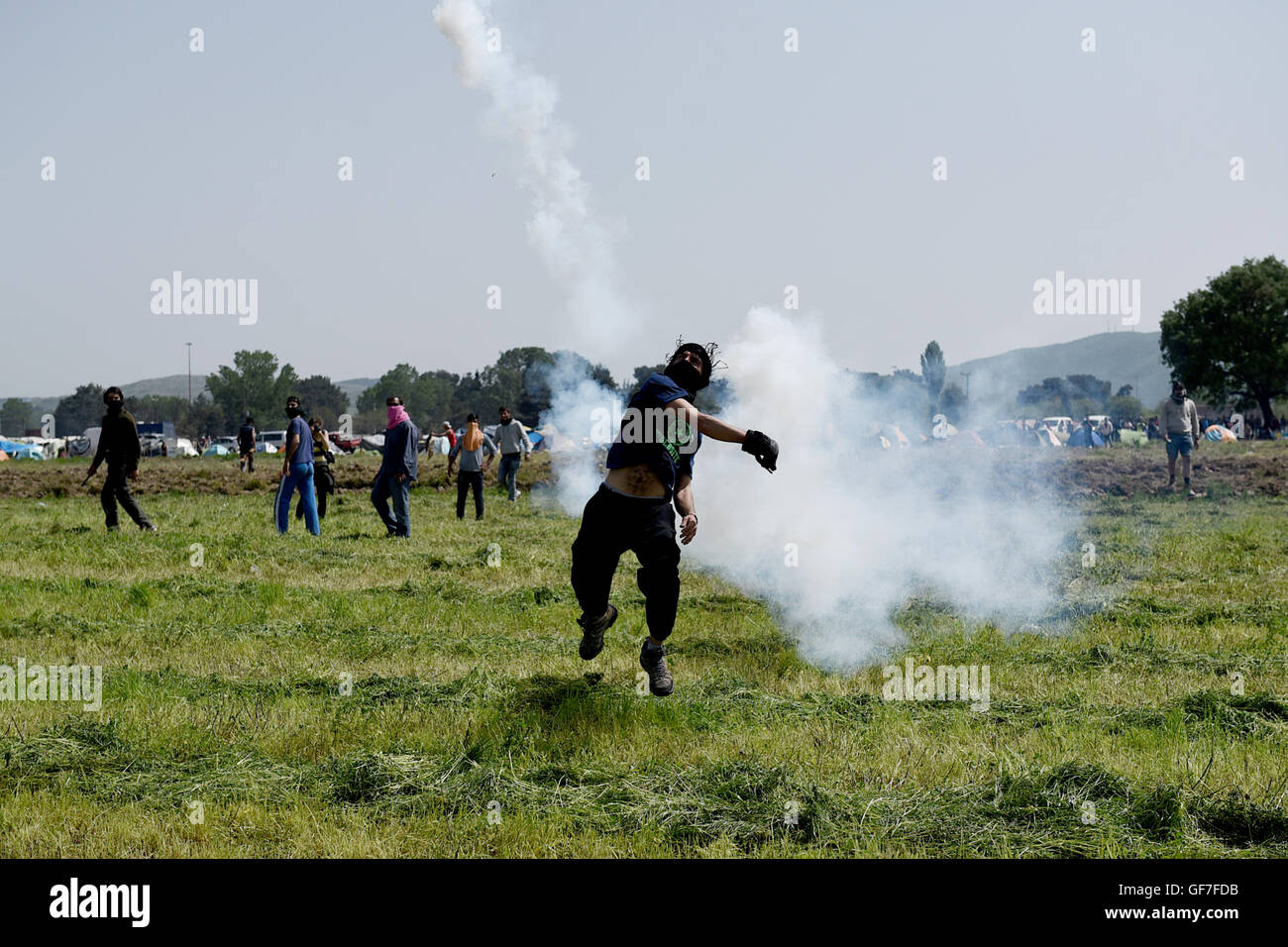 Un uomo getta torna alla polizia macedone un gas lacrimogeni canister, come i migranti e i rifugiati si scontrano con la polizia macedone al Greco confine macedone, vicino del nord del villaggio greco di Idomeni Foto Stock