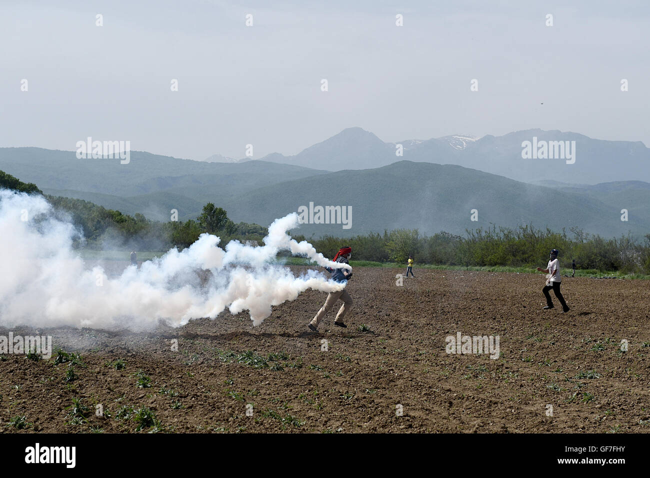 Un uomo getta torna alla polizia macedone un gas lacrimogeni canister, come i migranti e i rifugiati si scontrano con la polizia macedone al Greco confine macedone, vicino del nord del villaggio greco di Idomeni Foto Stock