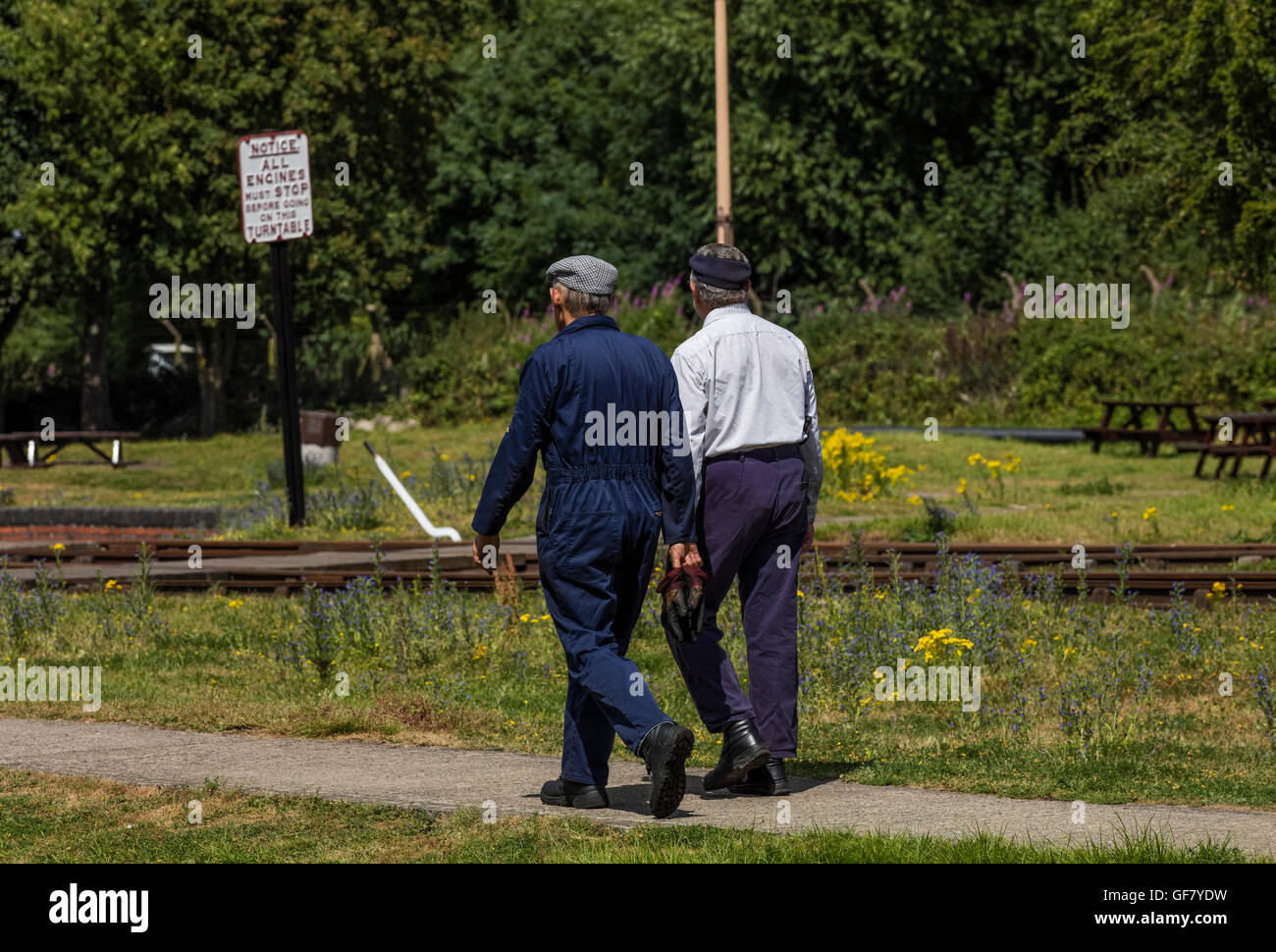 Due volontari camminano lungo un percorso verso il binario ferroviario e un segno al Didcot Railway Centre in Oxfordshire Foto Stock