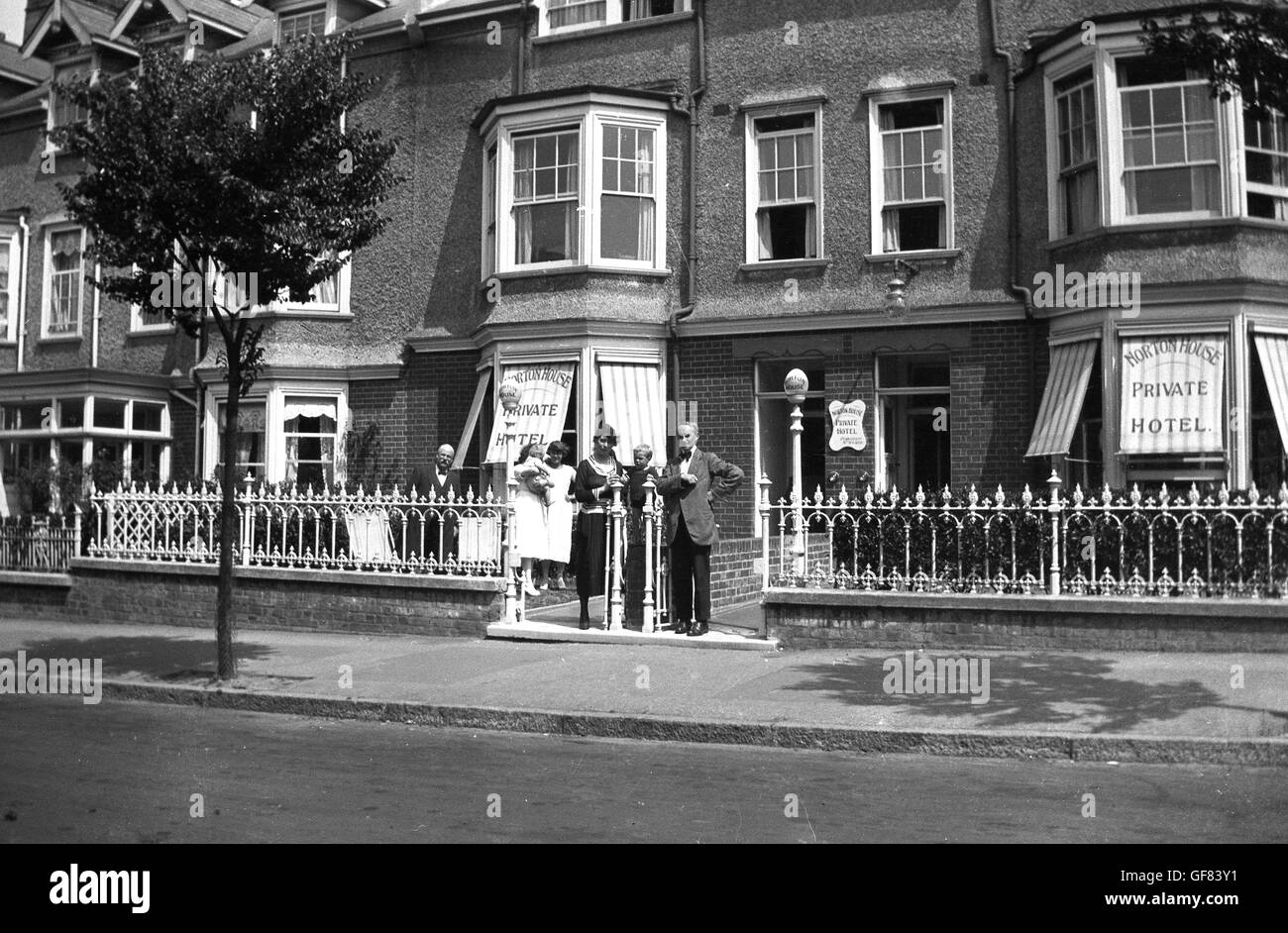Anni '30, storico, fuori da una fila di case a schiera vittoriane, diversi ospiti che si trovano all'ingresso di Norton House, un hotel o pensione di proprietà privata e gestito in una strada urbana, Inghilterra. Foto Stock