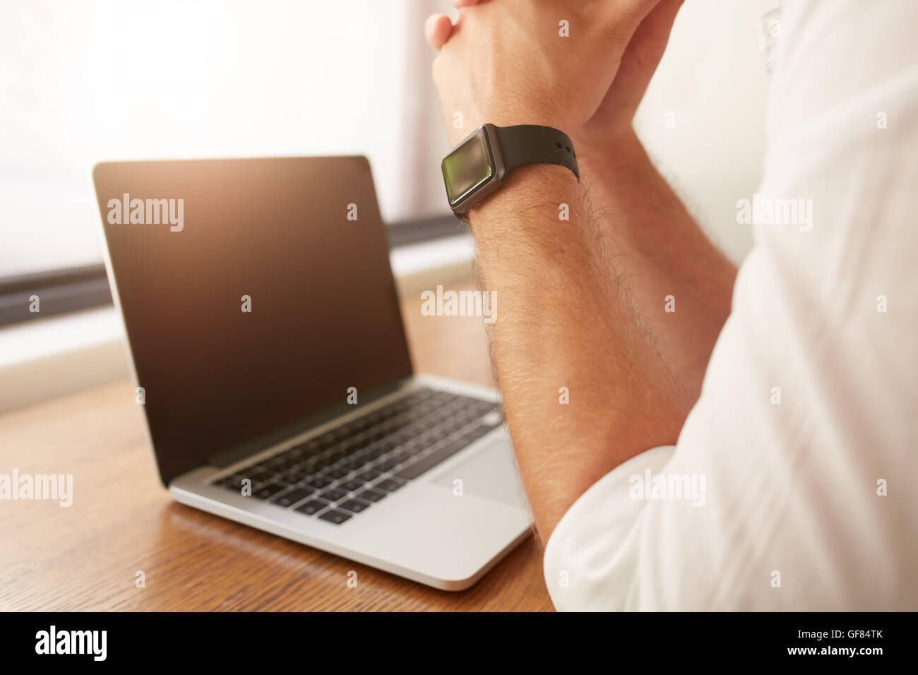 Close up dell'uomo seduto alla sua scrivania con computer portatile, indossa una smartwatch. Foto Stock