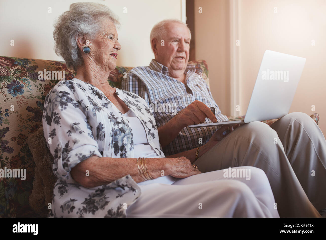 Piscina colpo di coppia senior seduta su un divano con un computer portatile. Il vecchio uomo e donna relax su un divano utilizzando laptop. Foto Stock