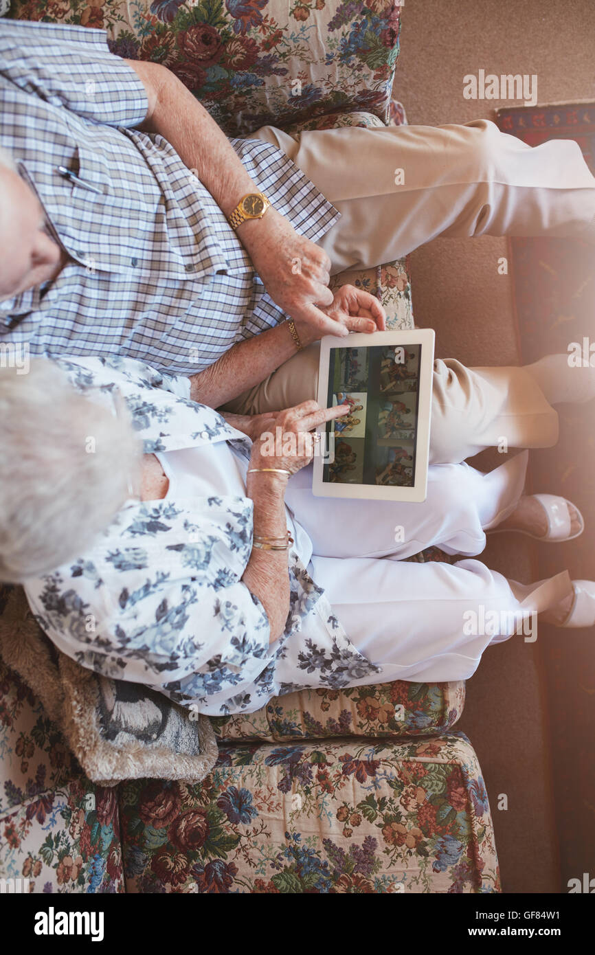 Vista superiore della coppia di anziani guardando le immagini sulla tavoletta digitale. Senior l uomo e la donna seduta sul divano guardando le immagini su touch s Foto Stock