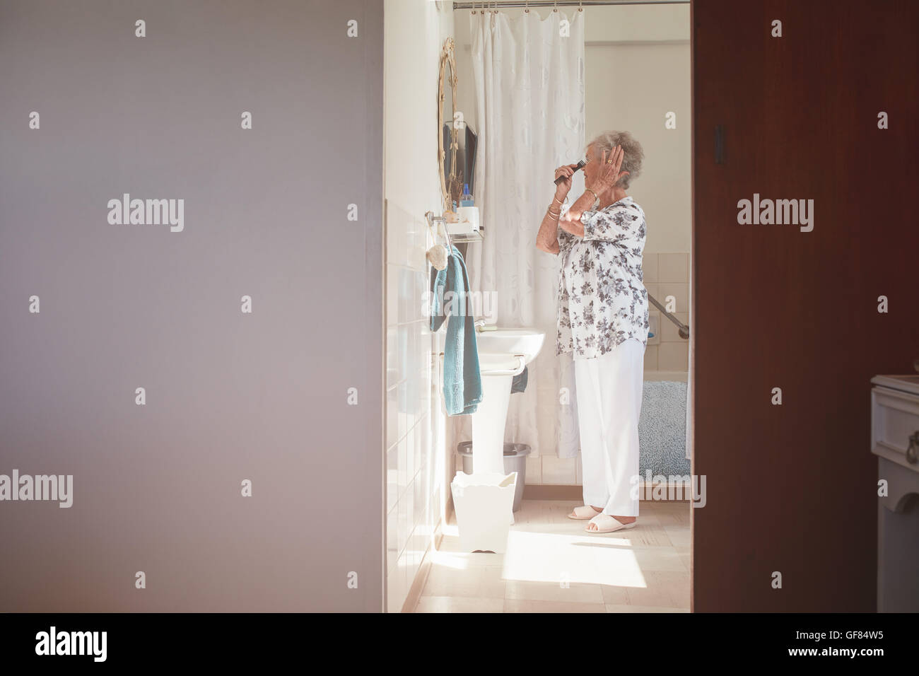 A piena lunghezza shot indoor di senior donna pettinare i capelli a cassettiera. Donna anziana prepararsi in bagno. Foto Stock