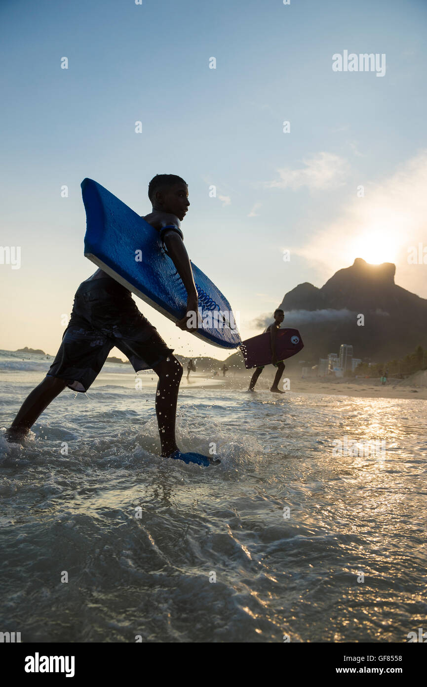 RIO DE JANEIRO - Marzo 8, 2016: Bodyboarders a piedi su São Conrado spiaggia sotto un tramonto della silhouette iconica Pedra da Gávea. Foto Stock