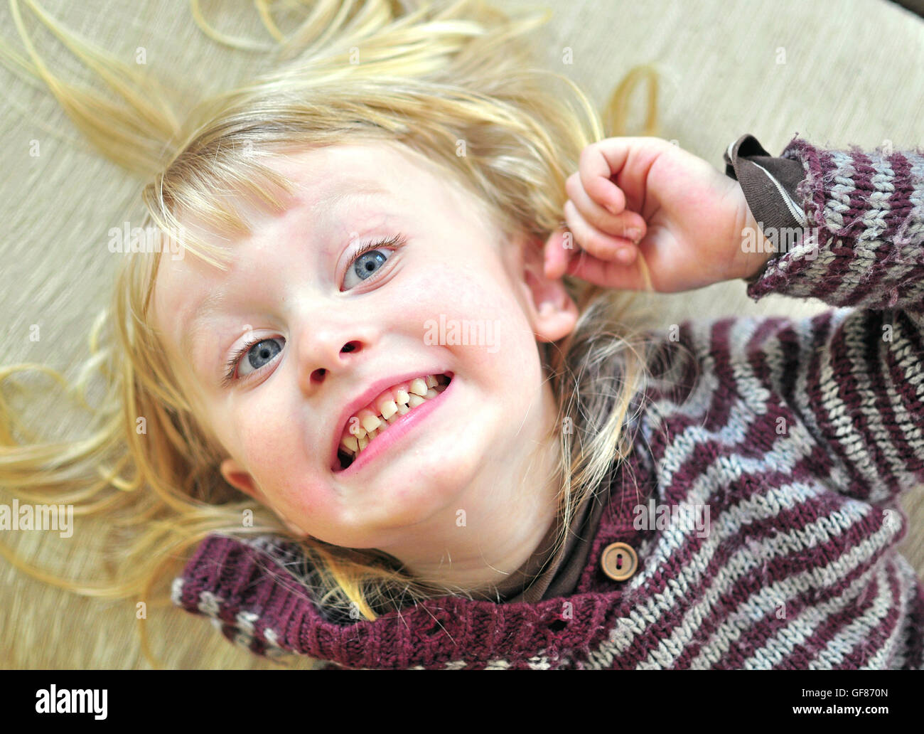 Carino sorridente bambino con una lunga capigliatura bionda giacente sul letto Foto Stock
