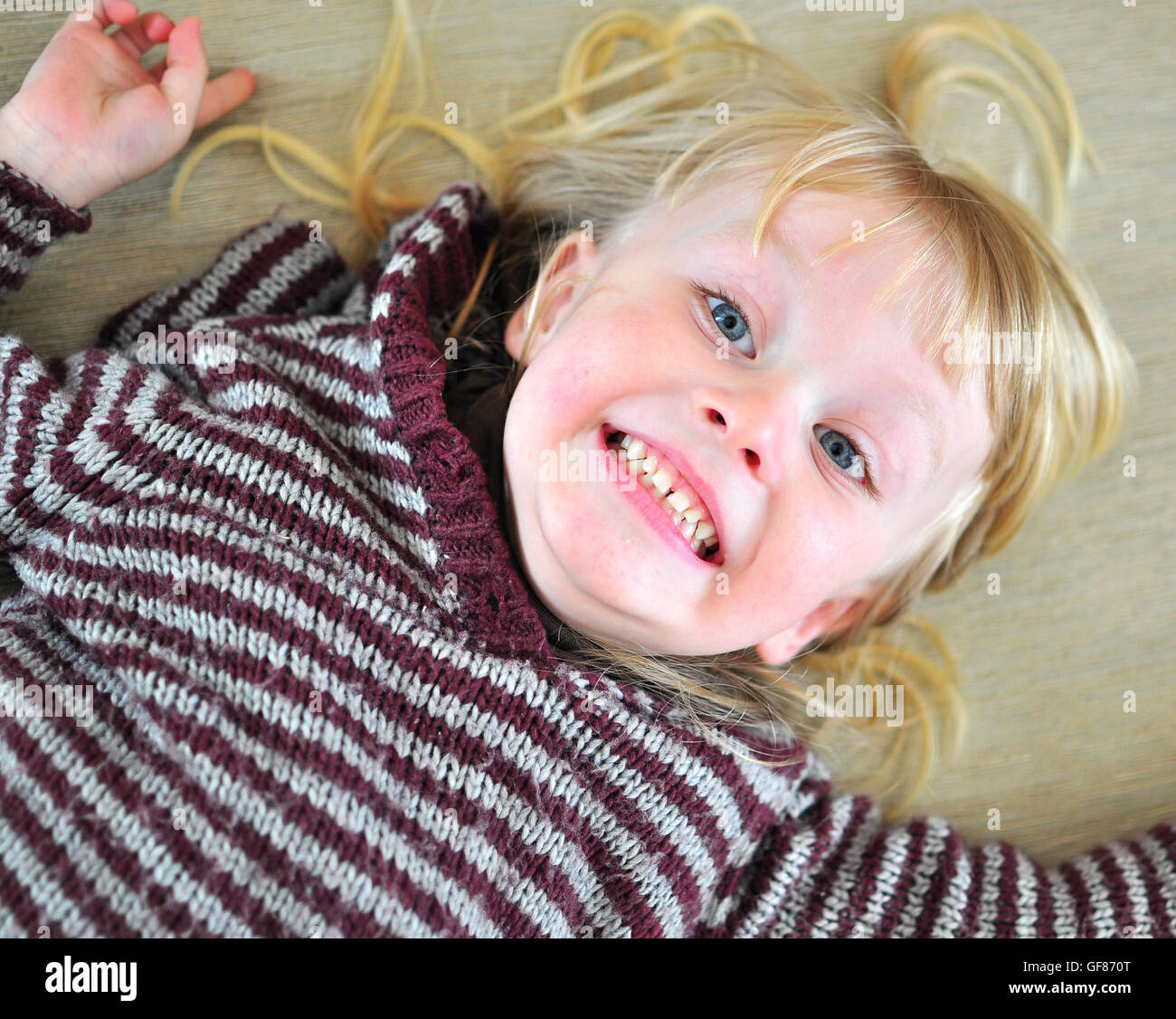 Carino sorridente bambino con una lunga capigliatura bionda giacente sul letto Foto Stock