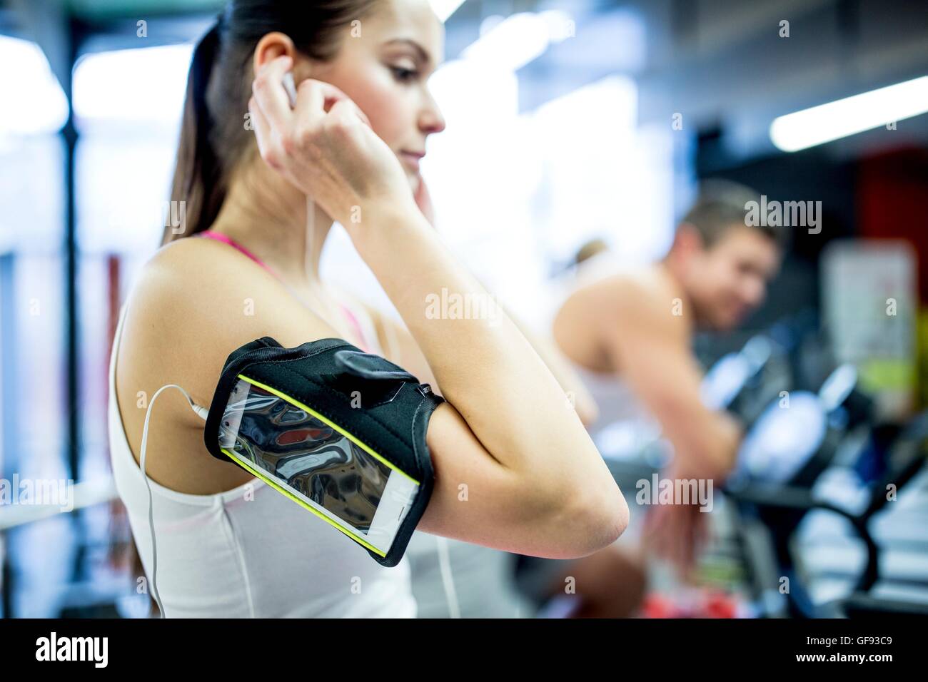 Proprietà rilasciato. Modello rilasciato. Giovane donna che indossa il braccio di regolazione della banda cuffie in palestra. Foto Stock