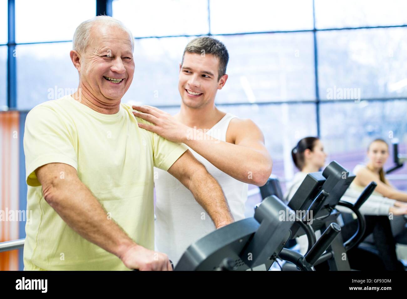 Proprietà rilasciato. Modello rilasciato. Giovane uomo assistere senior uomo mentre esercita sulla cyclette in palestra. Foto Stock