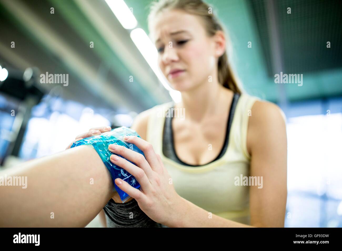 Proprietà rilasciato. Modello rilasciato. Giovane donna azienda confezione di ghiaccio sul ginocchio infortunato in palestra. Foto Stock