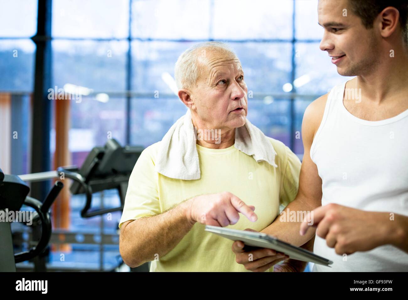 Proprietà rilasciato. Modello rilasciato. Giovani palestra trainer azienda digitale compressa e parlando con i senior uomo in palestra. Foto Stock