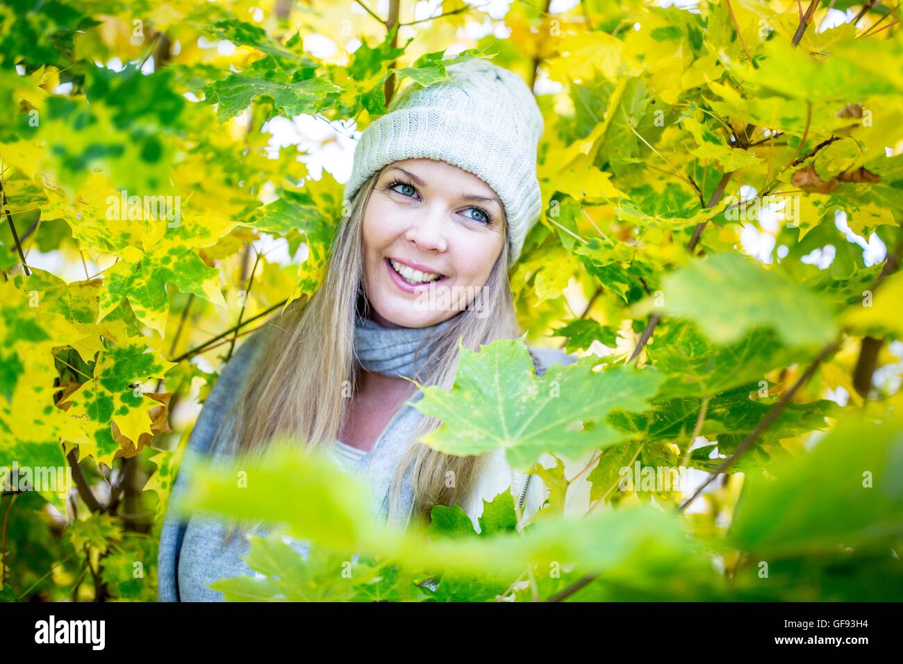 Modello rilasciato. Giovane donna sorridente mentre circondato da foglie di autunno. Foto Stock