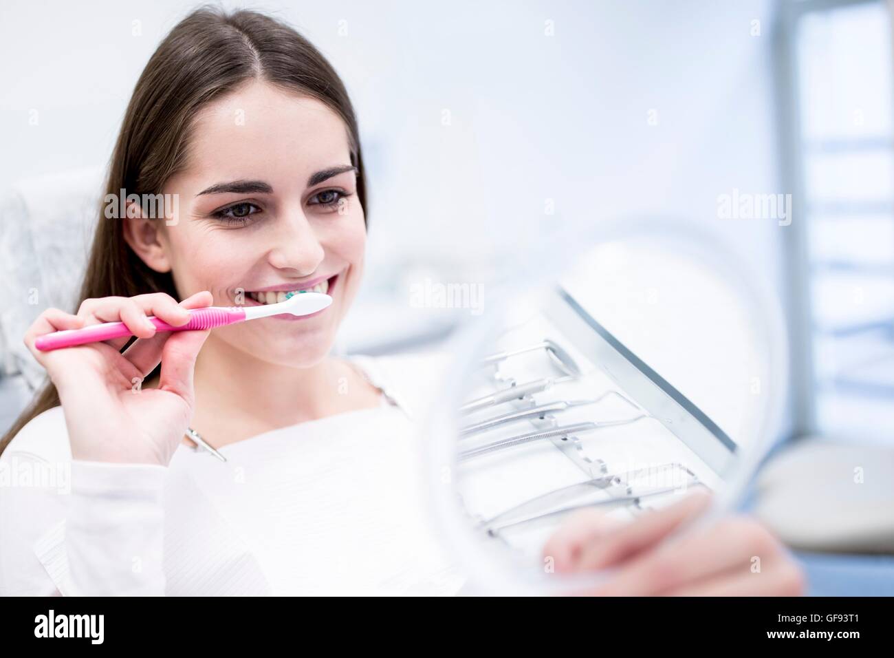 Modello rilasciato. Giovane donna spazzolatura dei denti e guardando la sua riflessione a specchio. Foto Stock