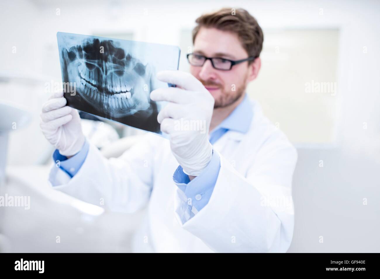 Modello rilasciato. Dentista guardando immagine a raggi x con assistenza dentale in background. Foto Stock