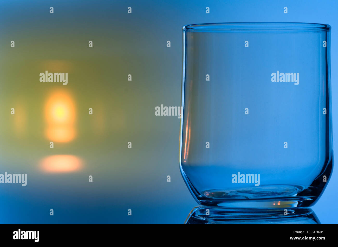 Nahaufnahme eines Trink-Glases vor blau angestrahlten Hintergrund mit gelben Reflex. Foto Stock