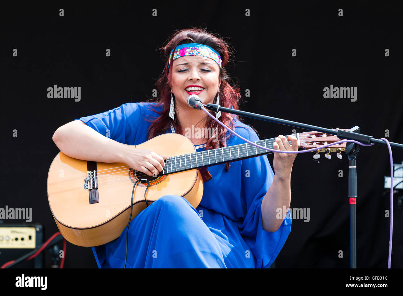 Columbian cantautore, cantante e chitarrista, Carolina Herrera in vestito blu, suonare la chitarra e cantare mentre è seduto su un palcoscenico open-air a Ramsgate. Foto Stock