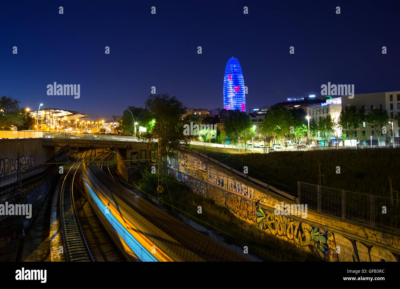 Vista urbano di Barcellona al crepuscolo con il treno in movimento in primo piano e la Torre Agbar (Gherkin) in background. Foto Stock