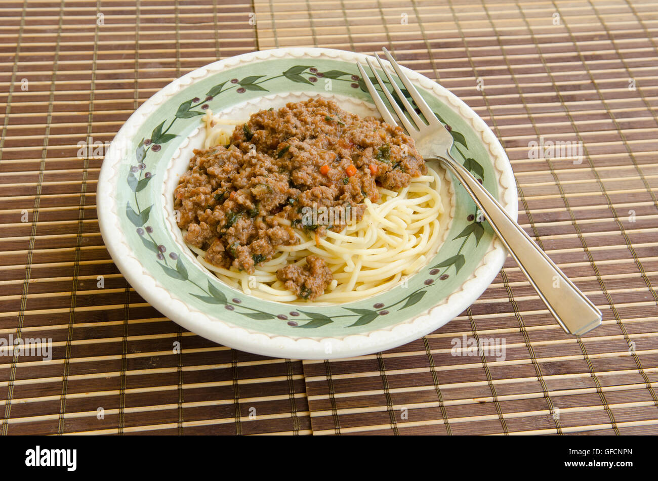 Spaghetti nella ciotola con il sugo di carne e la forcella sul tappetino di bambù Foto Stock