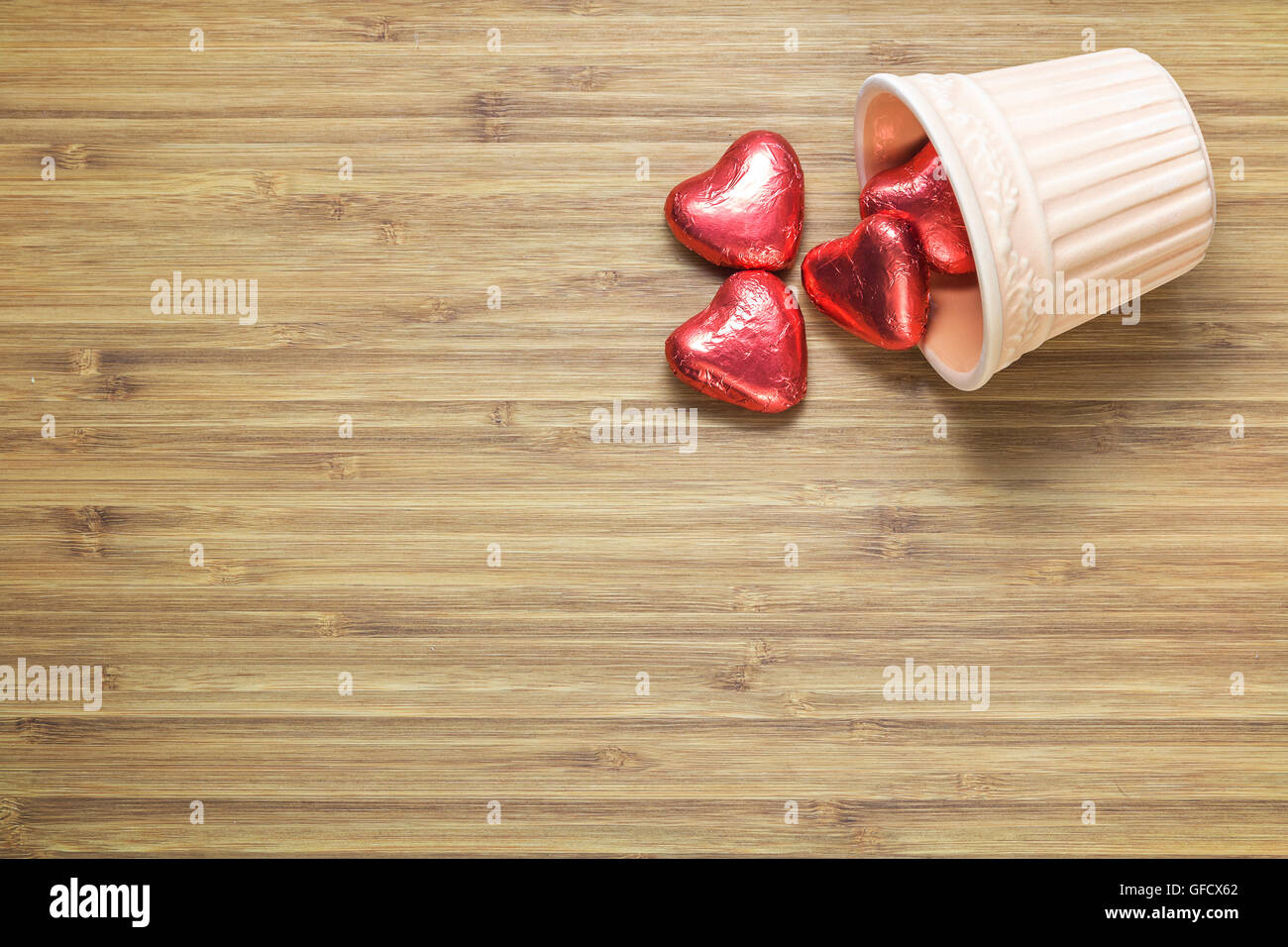 A forma di cuore ad caramelle confezionate in un colore rosso brillante  foil giacente in vaso di ceramica sulla texture di legno. Sfondo romantico  per i temi Foto stock - Alamy