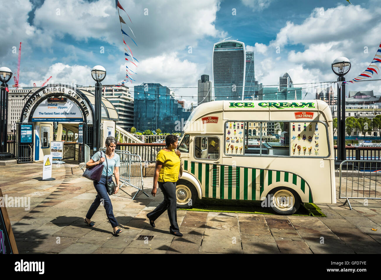 Due donne che camminano davanti a un furgone del gelato di fronte al molo di London Bridge City sul fiume Tamigi, Londra, Inghilterra, Regno Unito Foto Stock