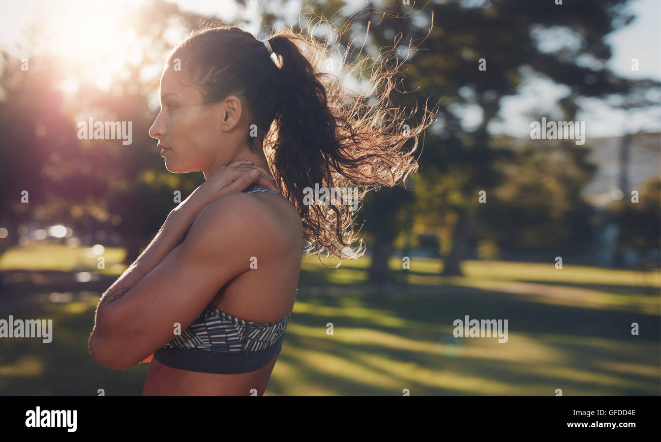 Vista laterale colpo di montare la giovane donna in piedi in un parco. Focalizzato giovane atleta femminile in piedi all'aperto sulla giornata di sole. Spazio copia ri Foto Stock