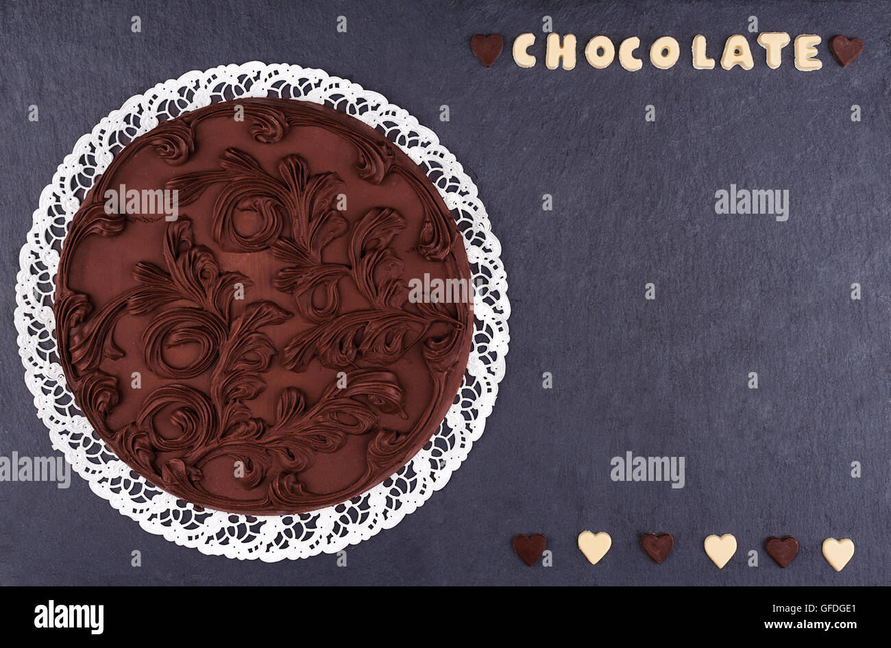 Round della torta di cioccolato su un scheda di ardesia vista dall'alto. Cioccolato Il cioccolato lettere con il testo di cioccolato e spazio di copia Foto Stock