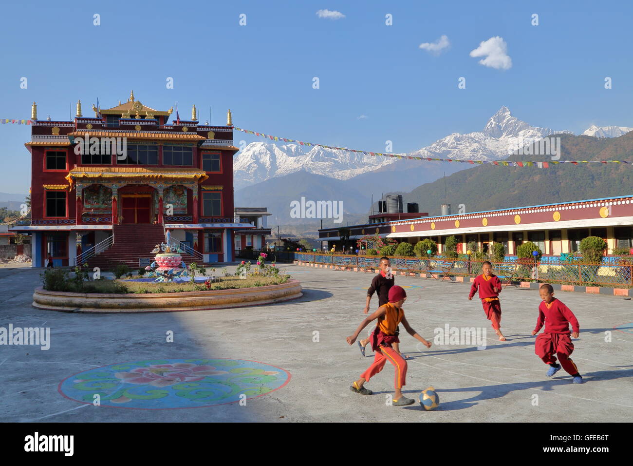 I monaci a giocare a calcio al di fuori di un tempio tibetano vicino a Pokhara, Nepal, l'Himalaya con picco di Machapuchare in background Foto Stock