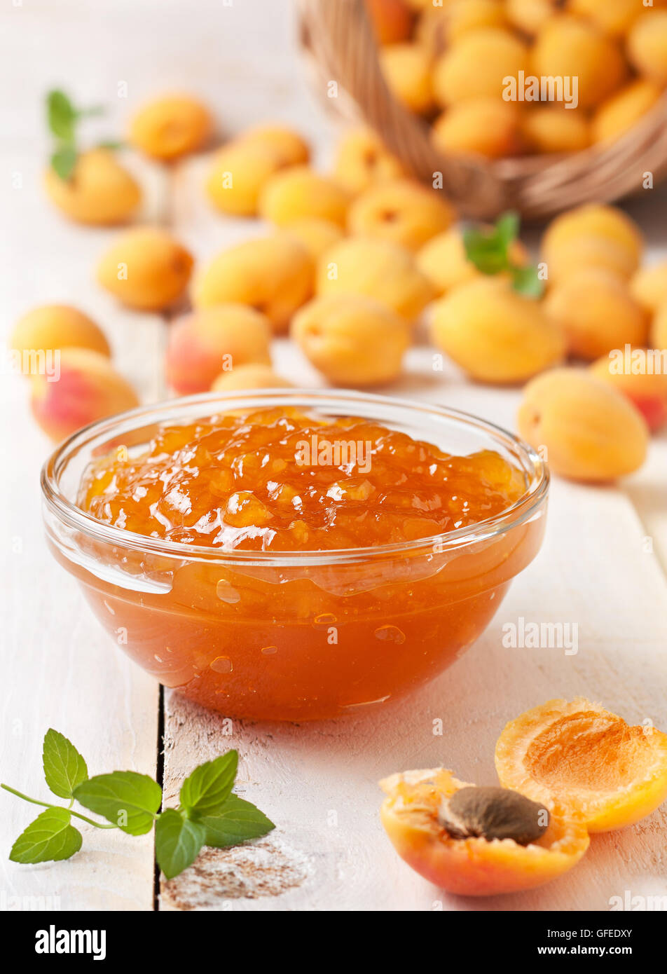 Confettura di albicocche in una ciotola di vetro, fresche Albicocche in un cesto su una luce sullo sfondo di legno Foto Stock