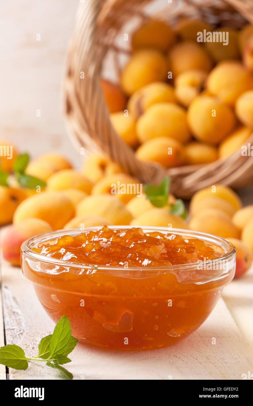 Confettura di albicocche in una ciotola di vetro, fresche Albicocche in un cesto su una luce sullo sfondo di legno Foto Stock
