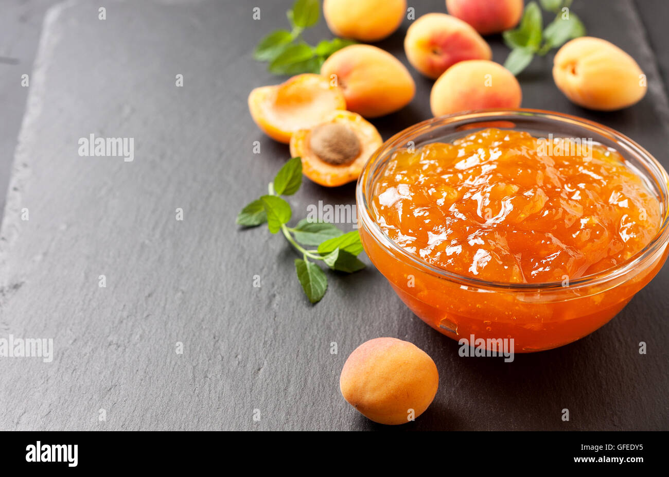 Confettura di albicocche in una ciotola di vetro, fresche Albicocche sulla pietra nera sullo sfondo Foto Stock