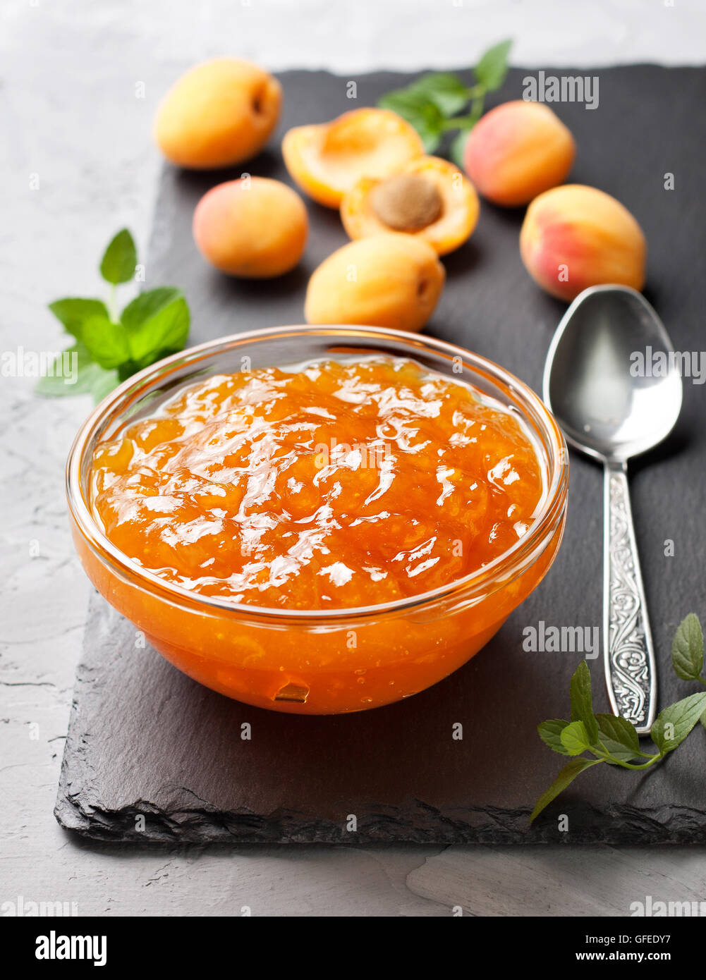 Confettura di albicocche in una ciotola di vetro, fresche Albicocche sulla pietra nera sullo sfondo Foto Stock