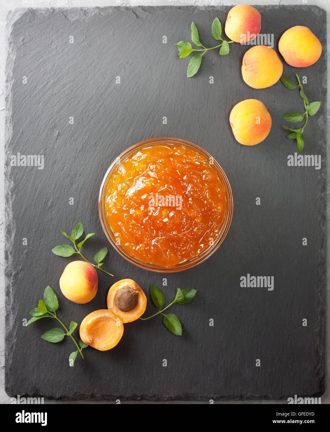 Confettura di albicocche in una ciotola di vetro, fresche Albicocche sulla pietra nera di sfondo (Vista superiore ) Foto Stock