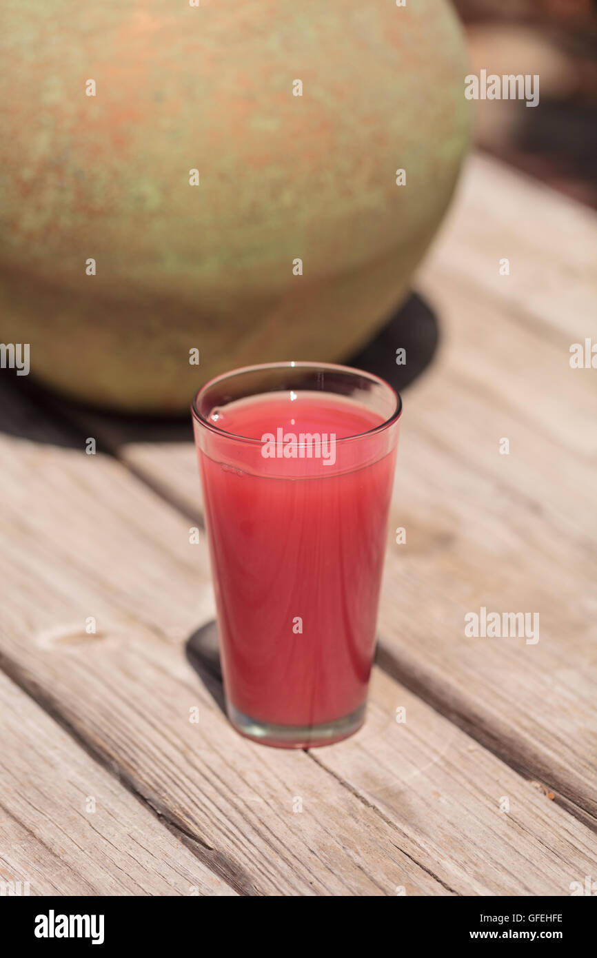 Vetro rosa di rosso anguria succo di frutta da bere in estate su un rustico tavolo da picnic. Foto Stock