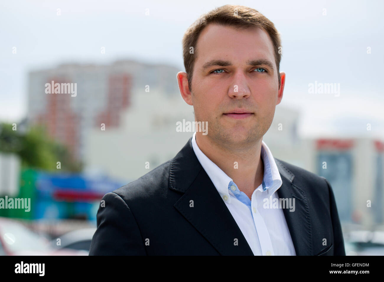 Close-up ritratto di un giovane uomo di affari in un abito scuro e camicia bianca sullo sfondo della città di estate Foto Stock