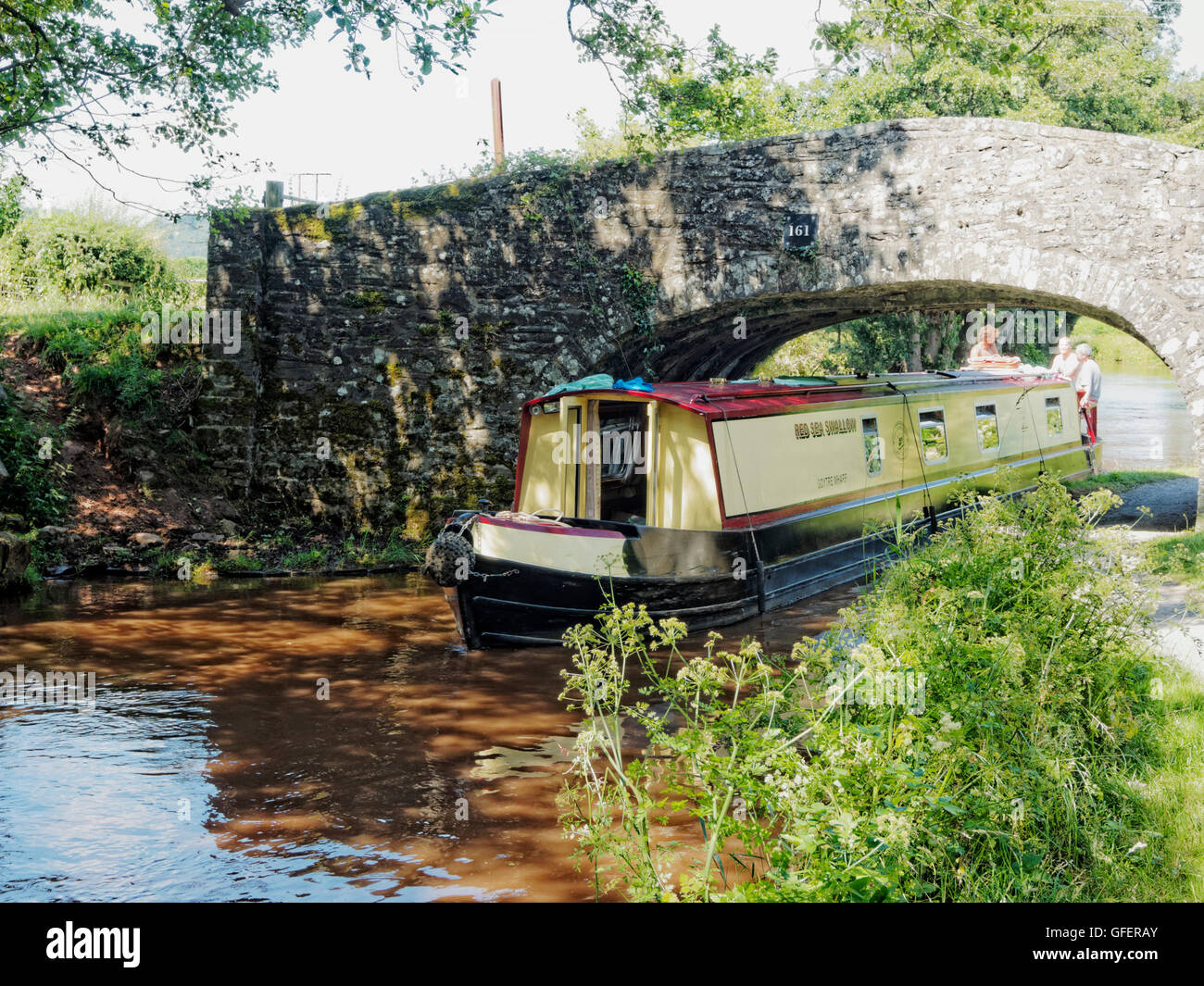 Holiday noleggio barca stretta passa attraverso un caratteristico ponte in pietra sulla Monmouth e Brecon Canal vicino Pencelli, Galles Foto Stock