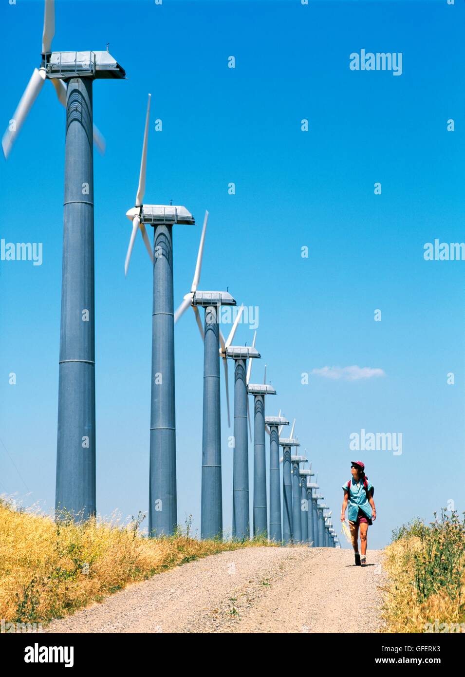 Donna che cammina sulla via accanto a turbine eoliche, parte del massiccio di wind farm complesso ad Altamont vicino Livermore, California, Stati Uniti d'America Foto Stock