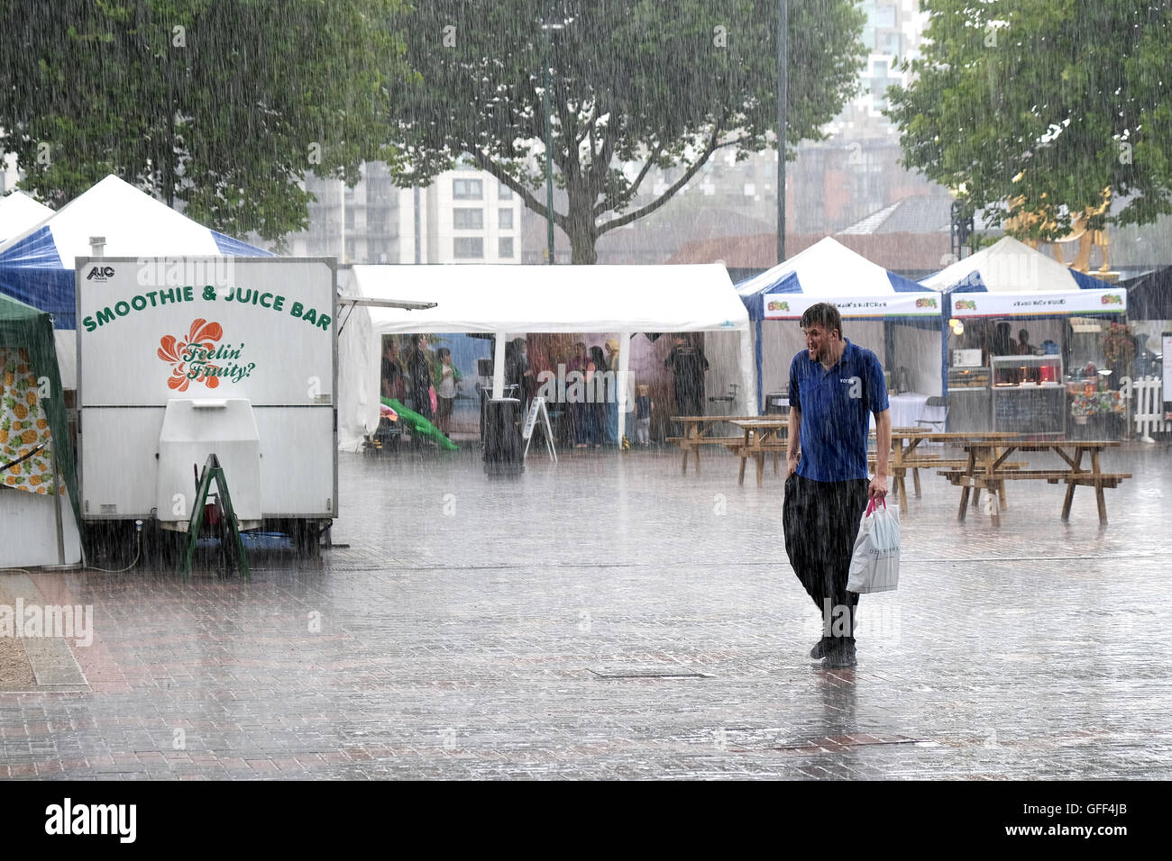 Un maschio shopper passeggiate attraverso una zona pedonale sotto la pioggia battente avente stati catturati fuori bu un improvviso temporale estivo Foto Stock