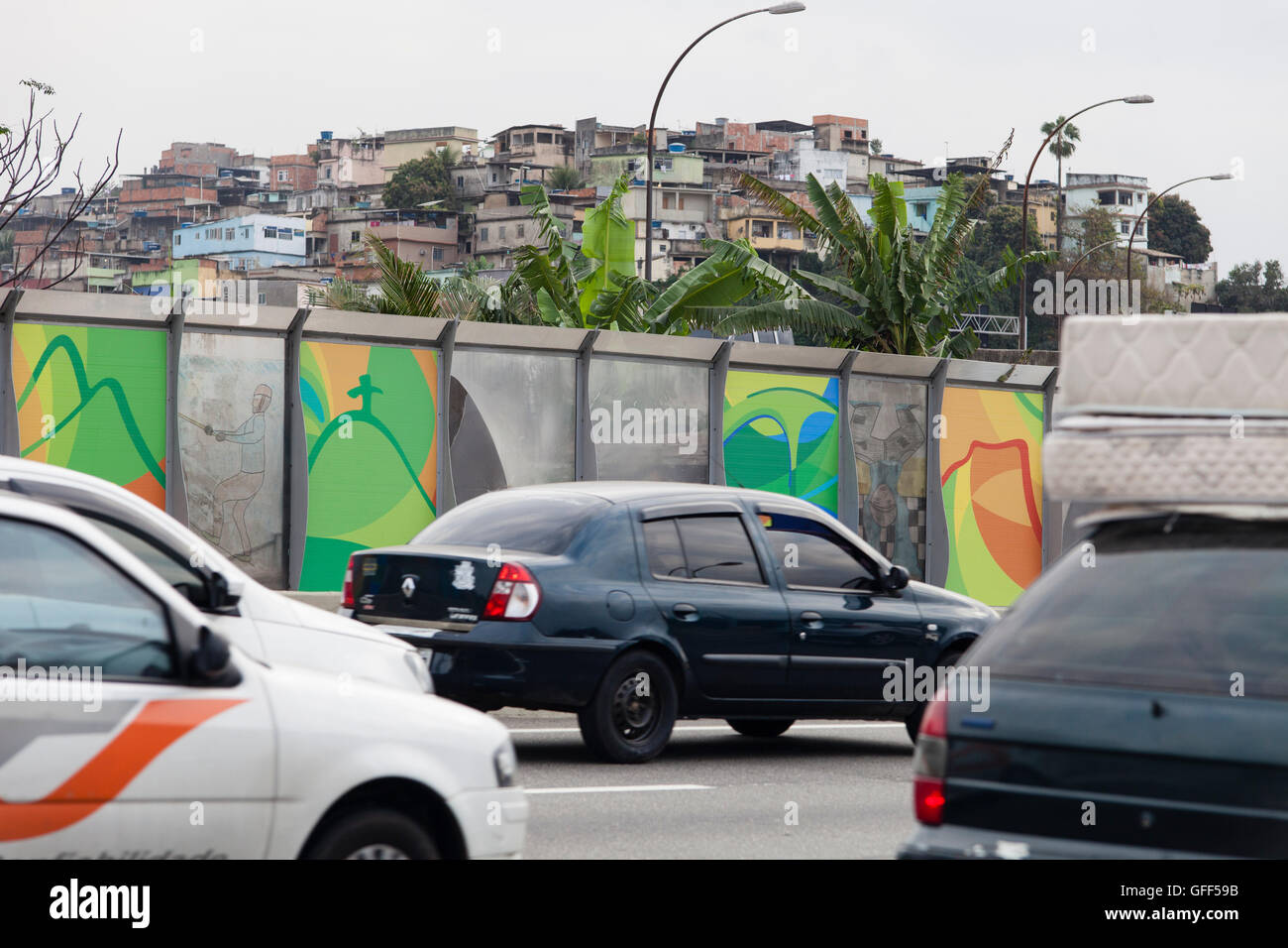 Complexo da mare, un enorme rete di favelas che affiancano la Linha Vermelha ( Linea Rossa ), la principale autostrada per l'aeroporto internazionale di Rio de Janeiro al centro della città - a partire dal 2010 la comunità è stata recintata dall'autostrada da enormi pannelli di Perspex - secondo le autorità forniscono una barriera acustica, la gente del posto lo descrivono come un "muro della vergogna", un altro modo di nascondere i poveri. Appena prima dei Giochi Olimpici la città cominciò intonacando i 3 metri di altezza, 7km del tratto di pannelli con colorati manifesti olimpici che mostra le principali della città paesaggi. Foto Stock