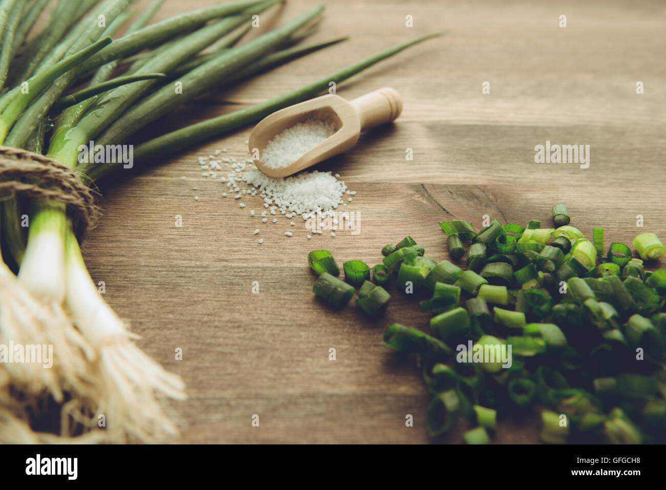 Un mazzetto di cipolline fresche shot a fianco di un cucchiaio di legno pieno di sale. In uno studio su una superficie di legno. Foto Stock