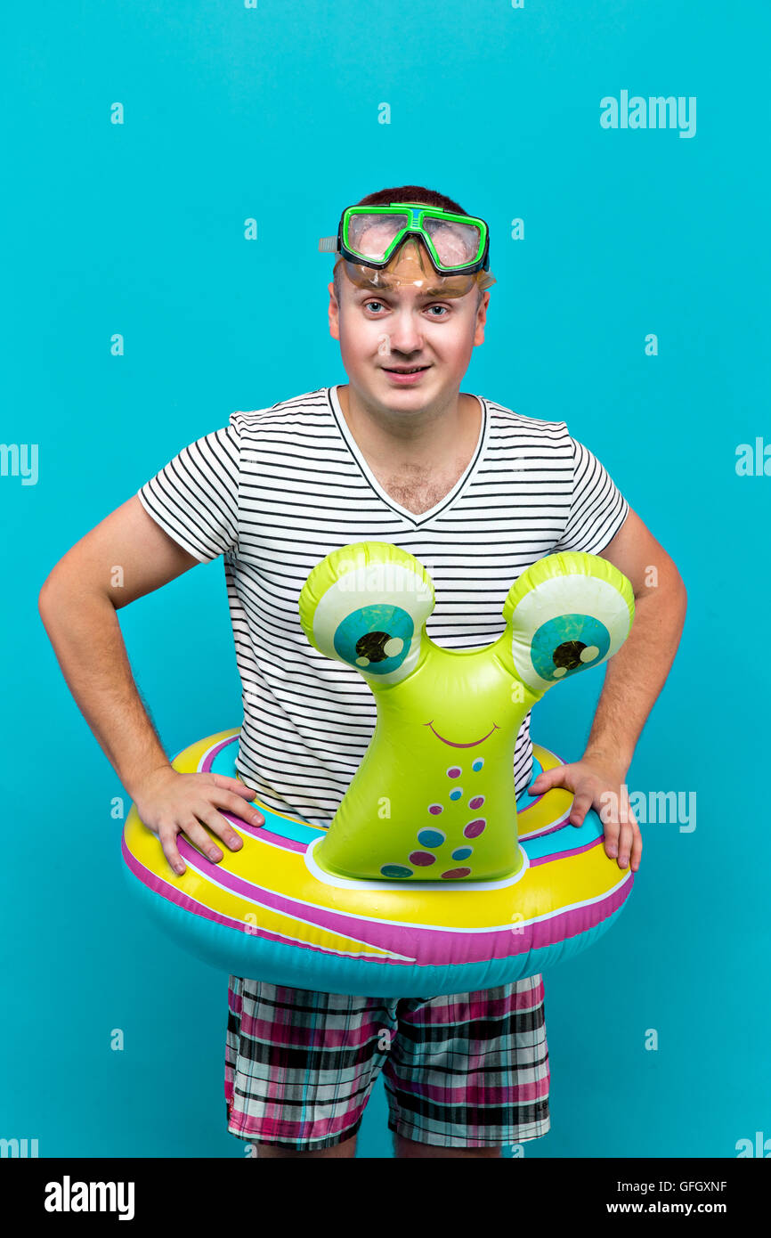 Uomo con una maschera subacquea, camicia a righe, nuoto giri in forma di una lumaca guardando nella telecamera, sfondo blu. Concetto di vacanza Foto Stock