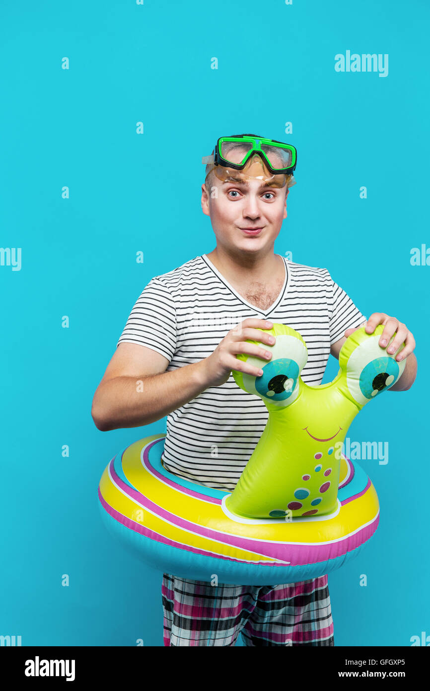 Uomo con una maschera subacquea, camicia a righe, nuoto giri in forma di una lumaca guardando nella telecamera, sfondo blu. Concetto di vacanza Foto Stock