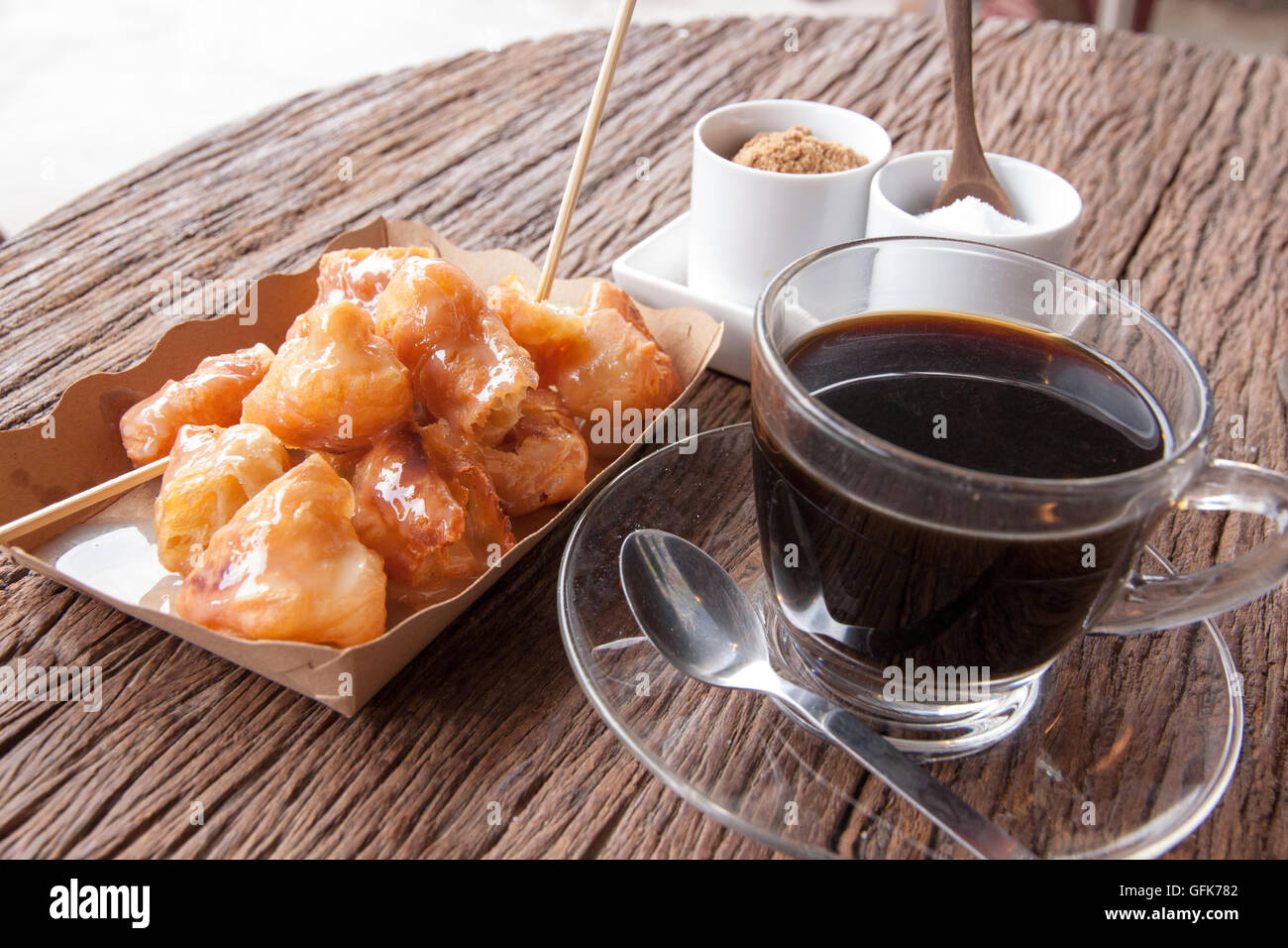 Fritte bastoncini di pasta in un piatto di carta e antichi caffè sul tavolo di legno in una mattinata Foto Stock