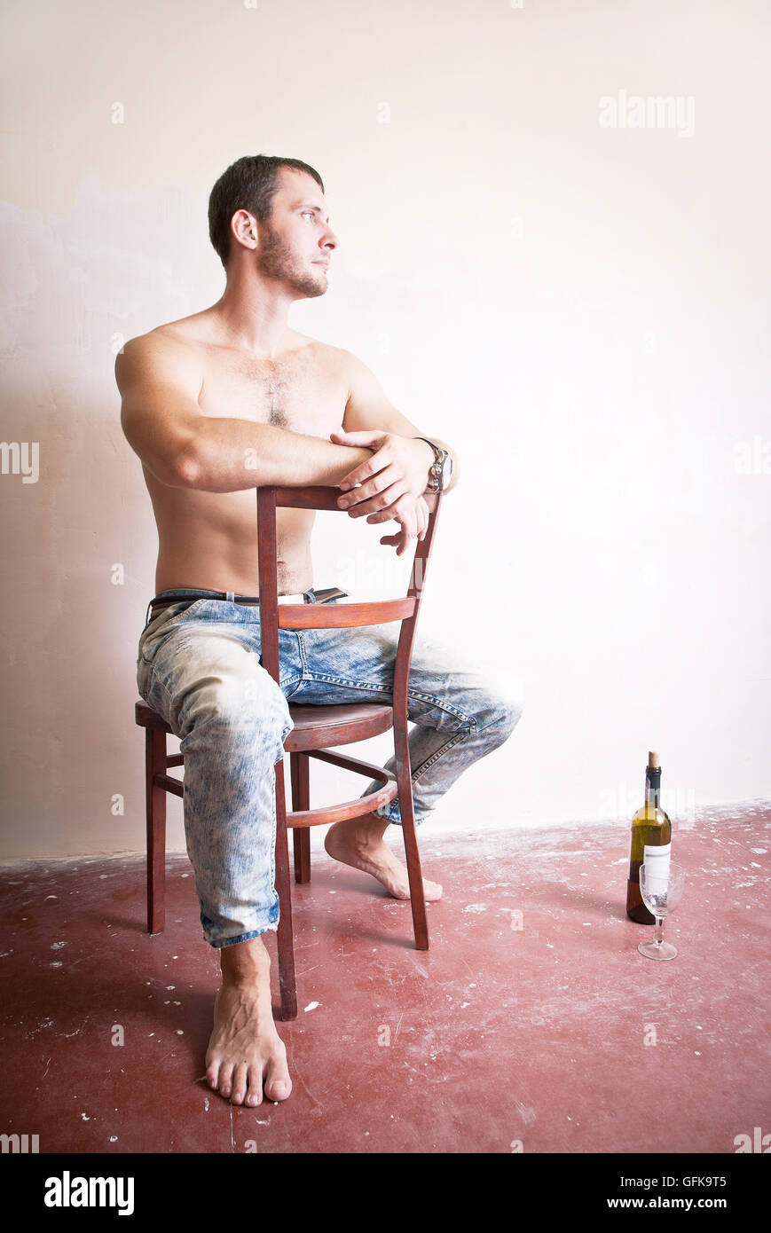 Uomo con una bottiglia di vino seduti su una sedia Foto Stock