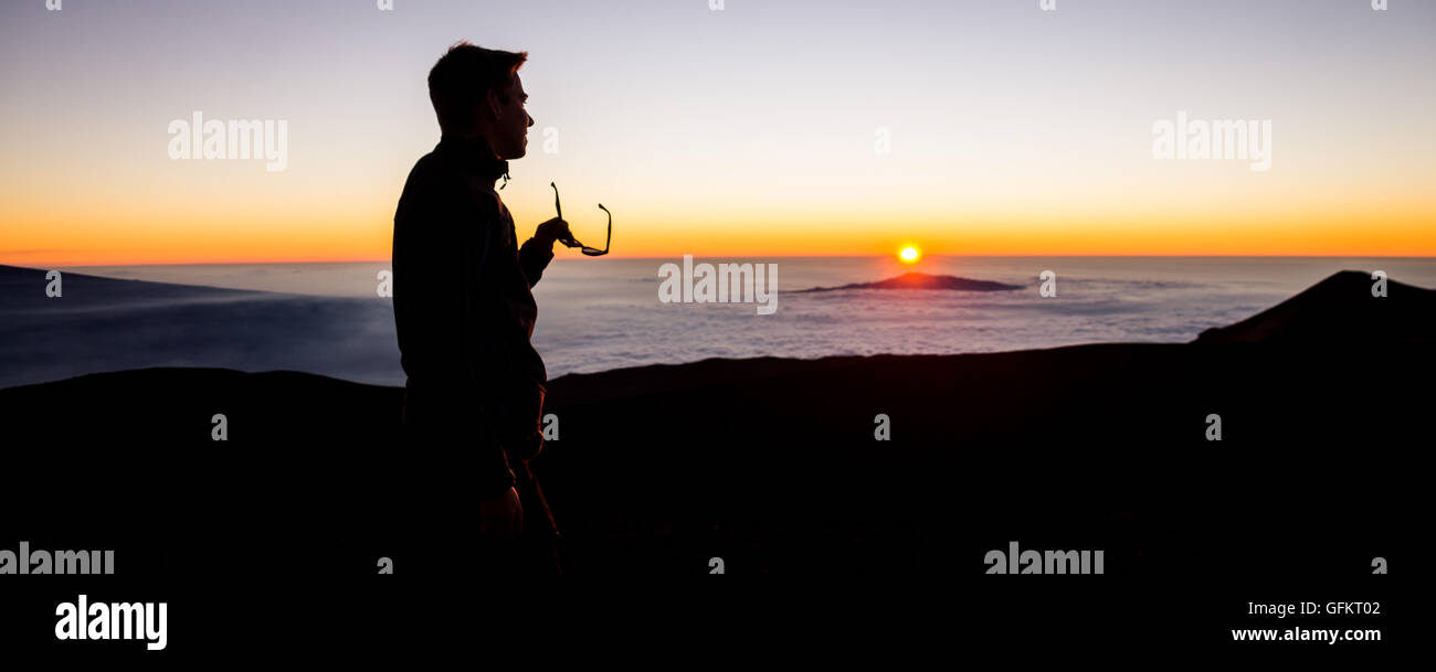 Persona di sesso maschile di decollare occhiali da sole per guardare il tramonto sopra le nuvole dal monte vulcano Mauna Kea sulla Big Island delle Hawaii, Foto Stock