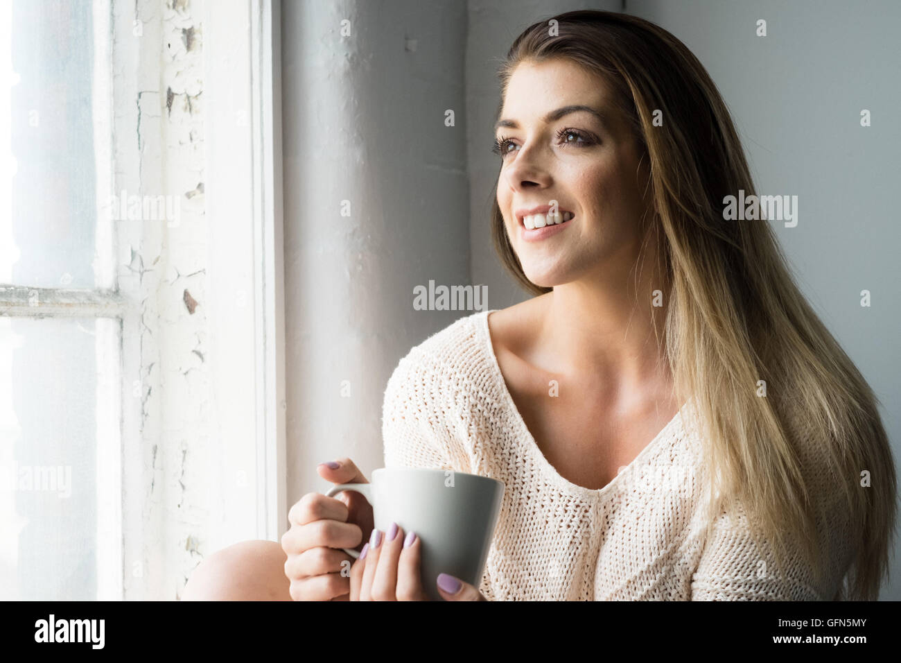 Donna sorridente guarda fuori della finestra. Foto Stock