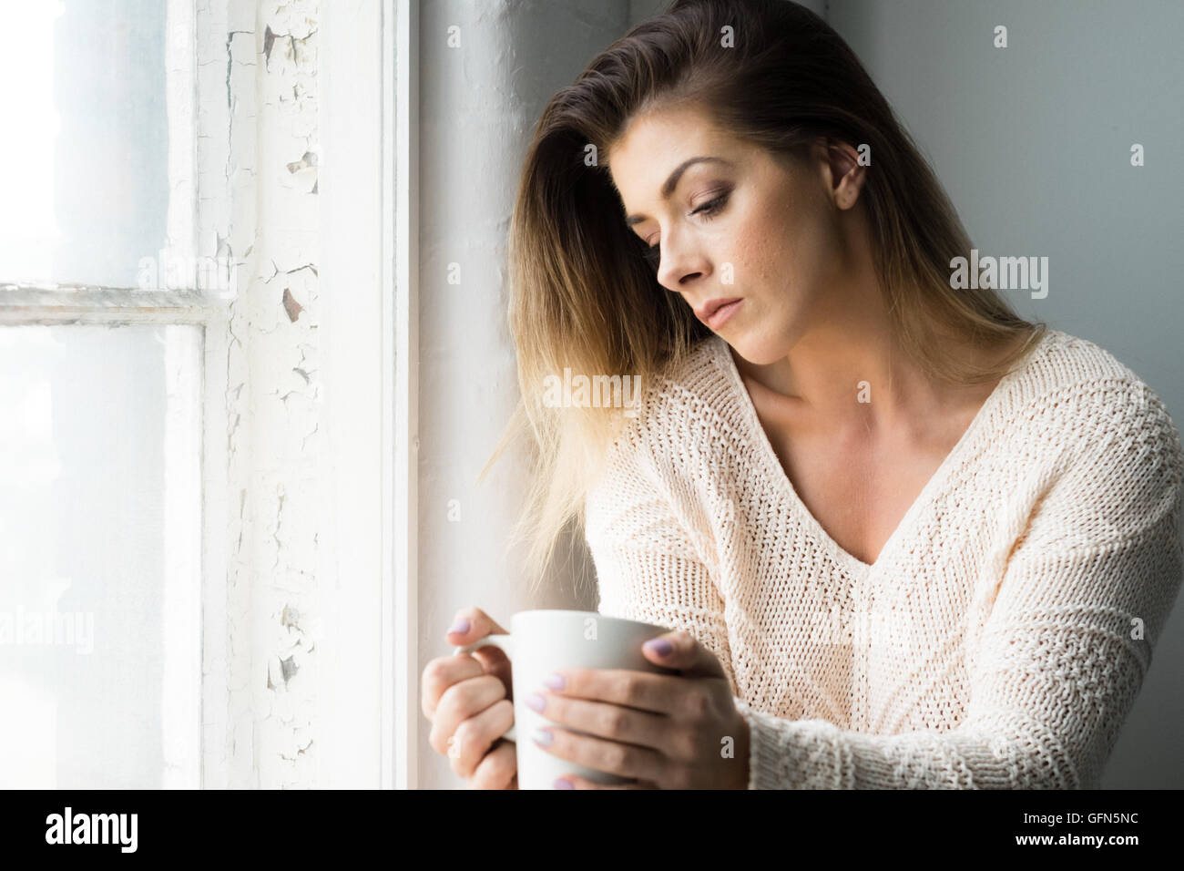 Donna nella sua 20s contempla la vita su una bevanda calda Foto Stock