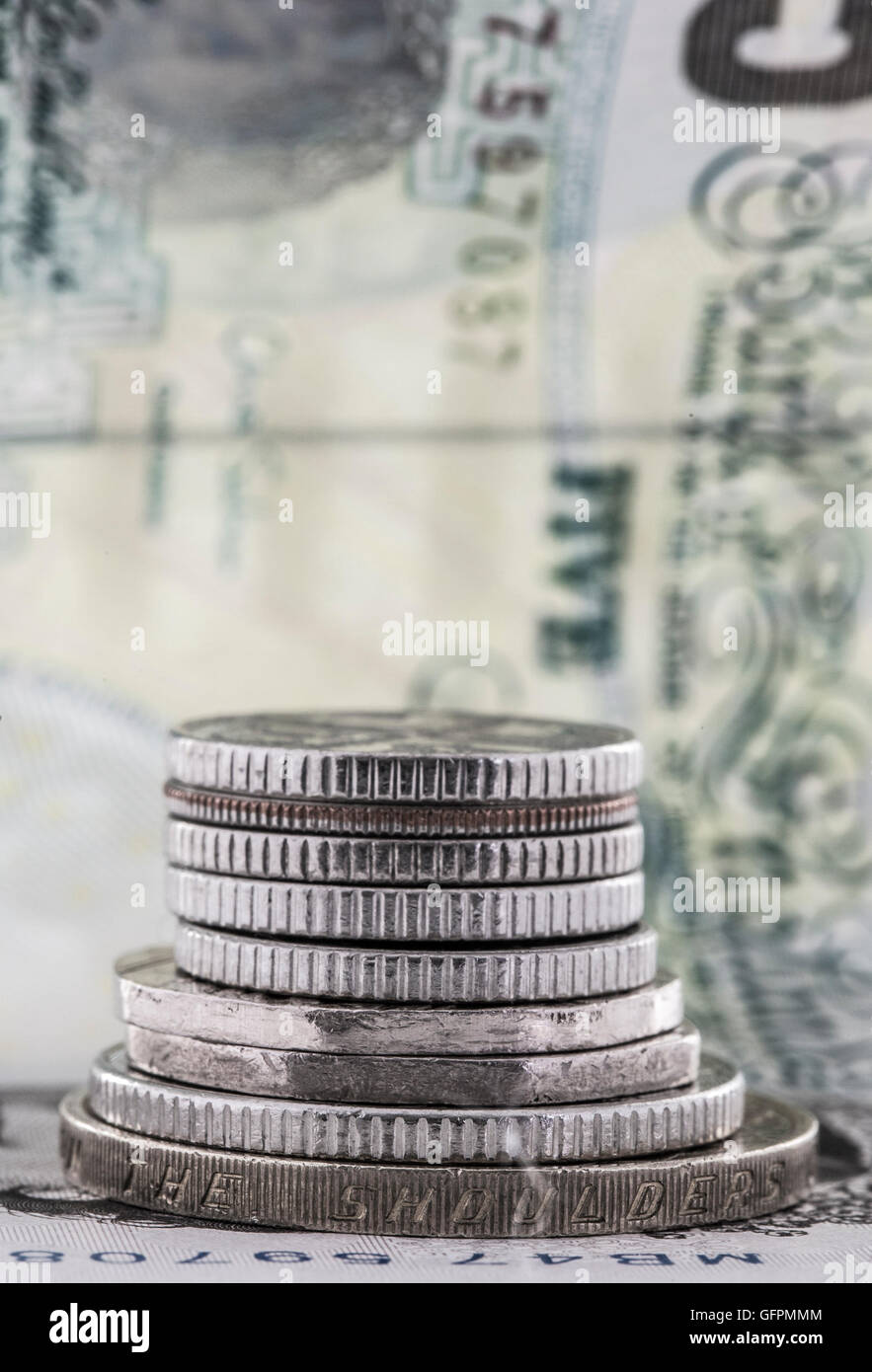 Pila di monete su uno sfondo di un £5 nota Foto Stock